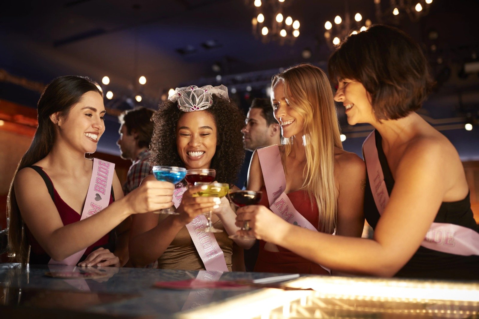 Bride-to-be and friends toasting with colorful cocktails in a nightclub, wearing party sashes, showcasing a lively bachelorette limo night out in DC.