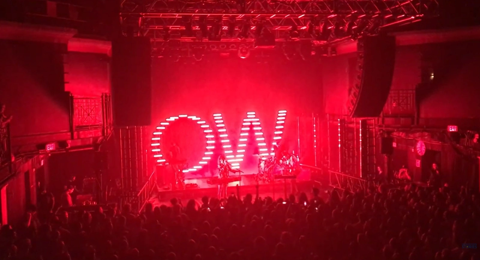 Concert performance under dynamic red lighting with an illuminated 'OW' sign, capturing the energy of the live music experience.