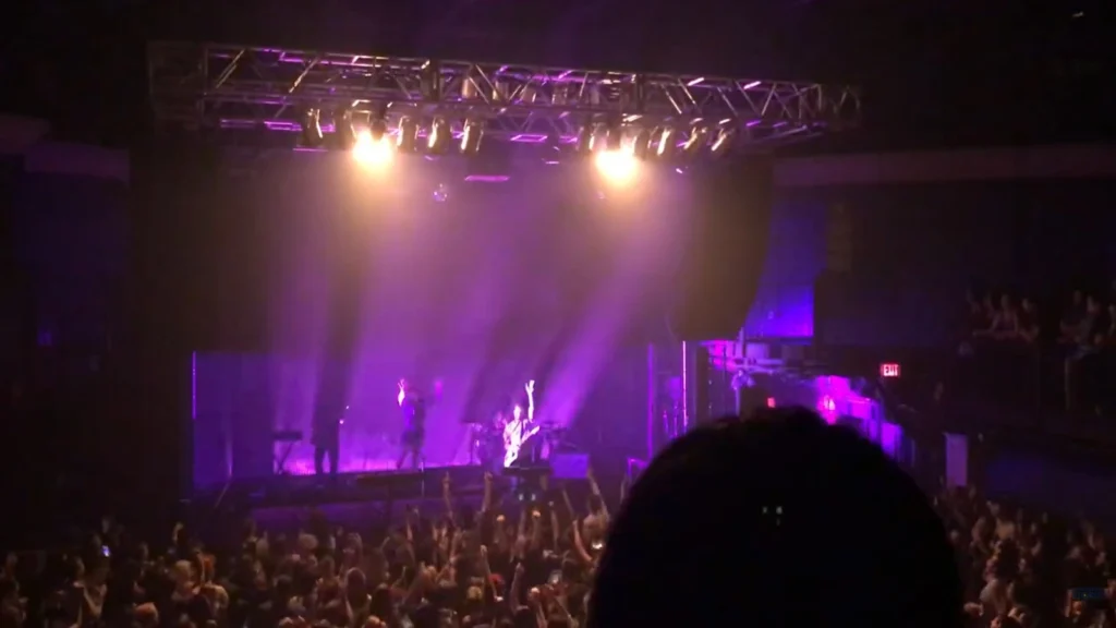 Exciting live concert scene with purple lighting and an enthusiastic crowd, highlighting the intense atmosphere of the performance.